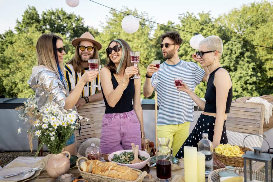 Five people holding beverages in a backyard next to a table of food