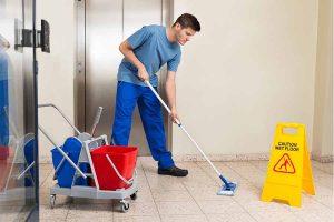 A man wearing a janitor uniform cleaning the floor.