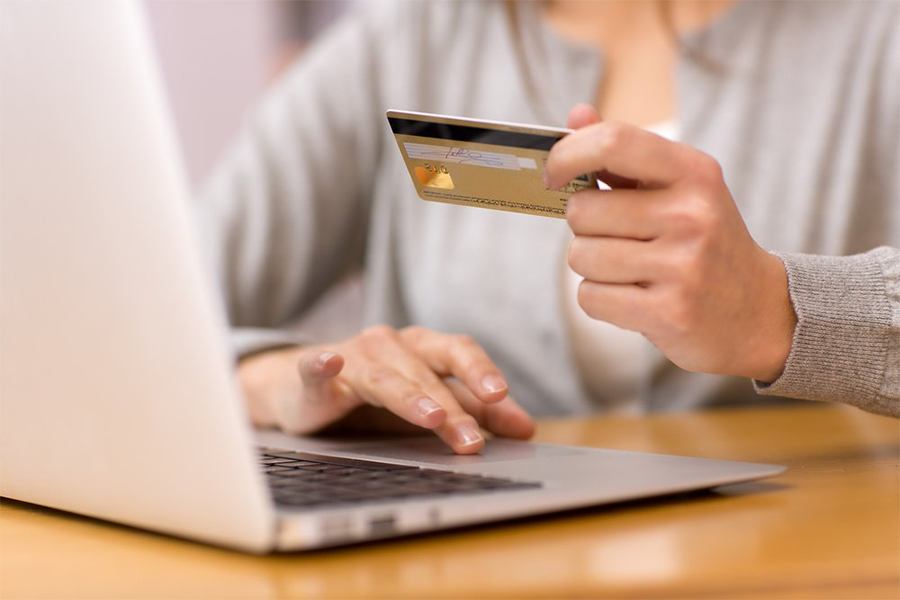 Woman's hand holding a credit card while browsing on her laptop.