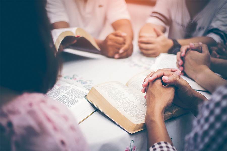 一群人把手放在桌子上做圣经研究。