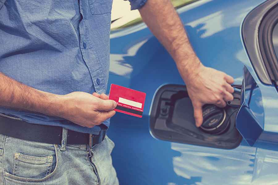 Man holding a fuel card beside a blue car.