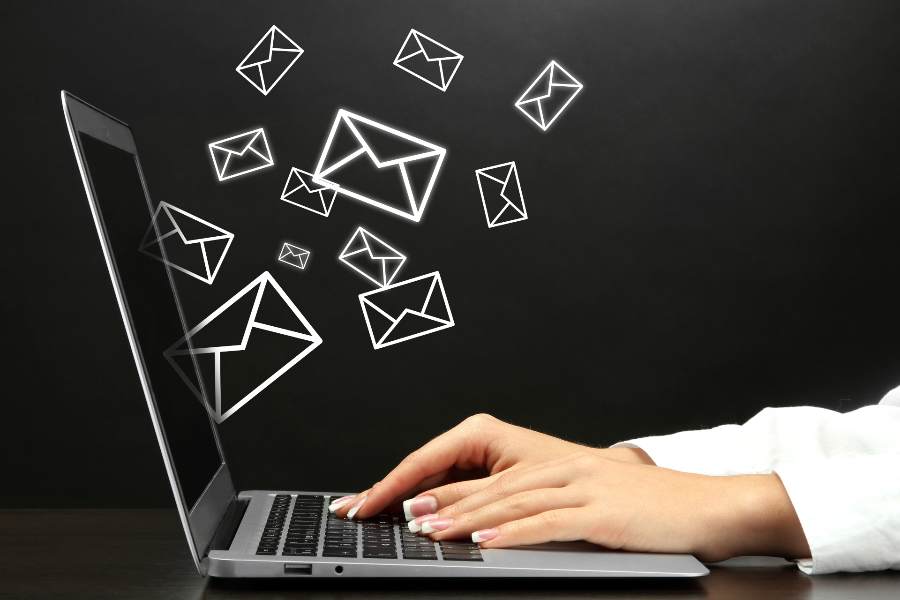 一个女人的手在笔记本电脑上打字，一些电子邮件图标从屏幕上飞了出来。