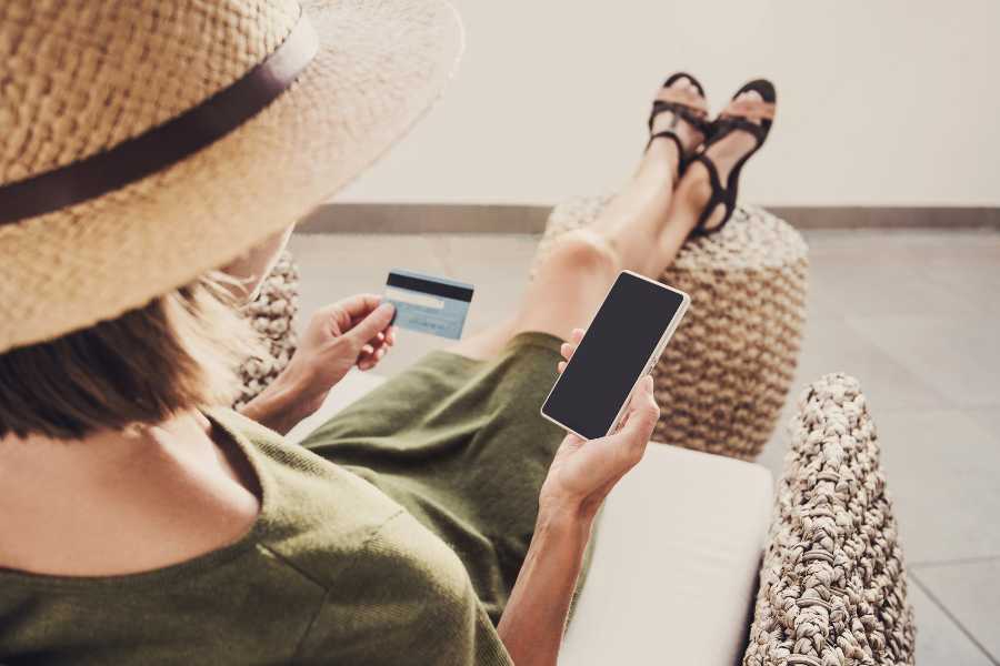Young woman on a vacation using a phone while holding a credit card.