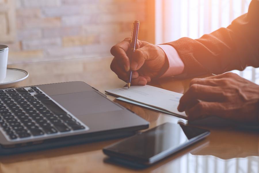 Business writing is writing in a check in front of his laptop and phone.