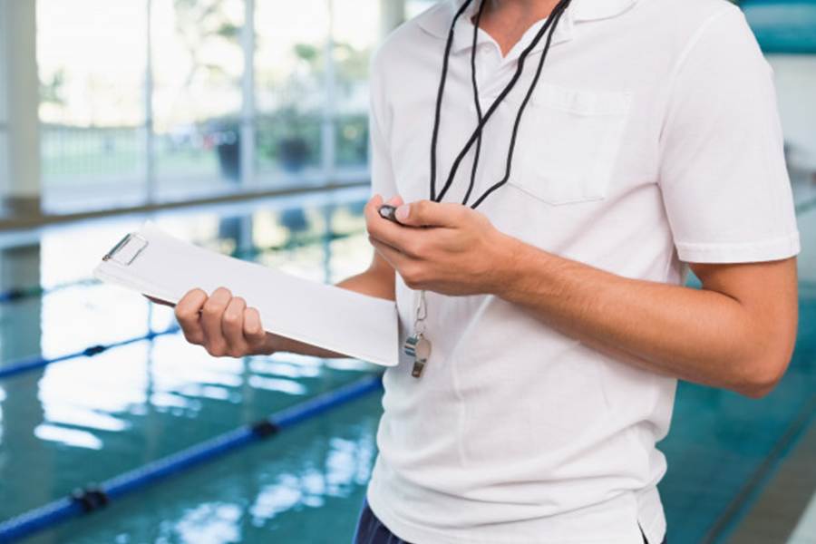 Male swimming coach holding a timer and a record book.