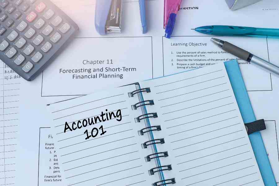 Accounting 101 written in small notebook with pens and calculator around it.
