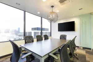 A meeting room with big windows, a television, and a lighting fixture hanging above the table.