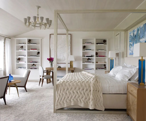 Staged bedroom with light neutral colors, sparse bookshelves, and carefully arranged furniture.