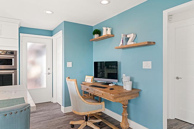 A home office with a blue accent wall, a computer monitor o a brown table, and open shelves