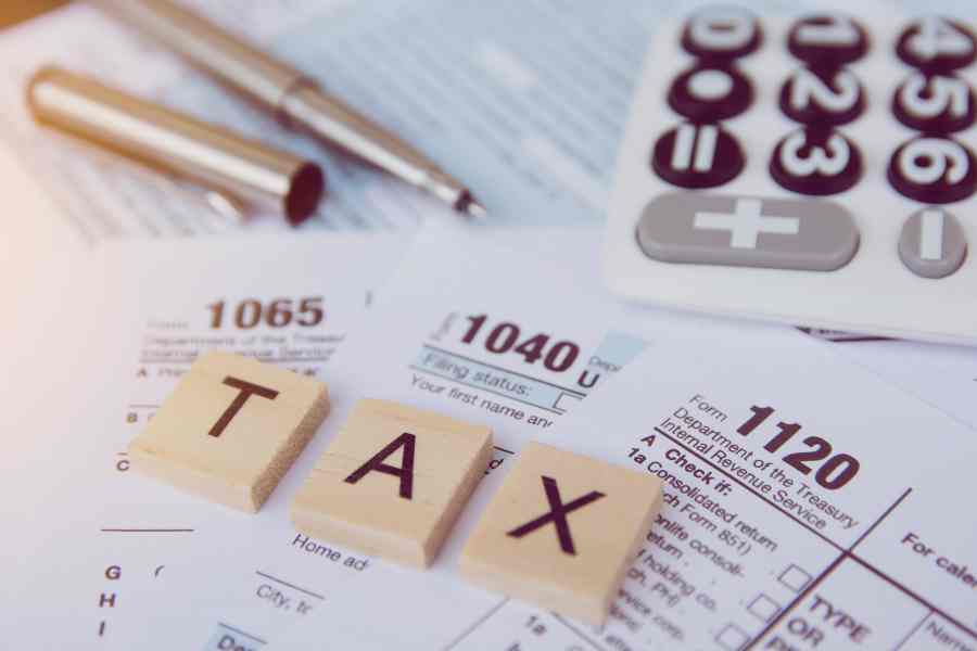 税务季节用木制字母块，计算器，笔在1040税表的背景。
