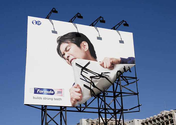 Formula toothpaste billboard with person biting off the billboard for slogan 