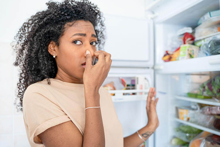 Woman holding her nose while opening a refrigerator.